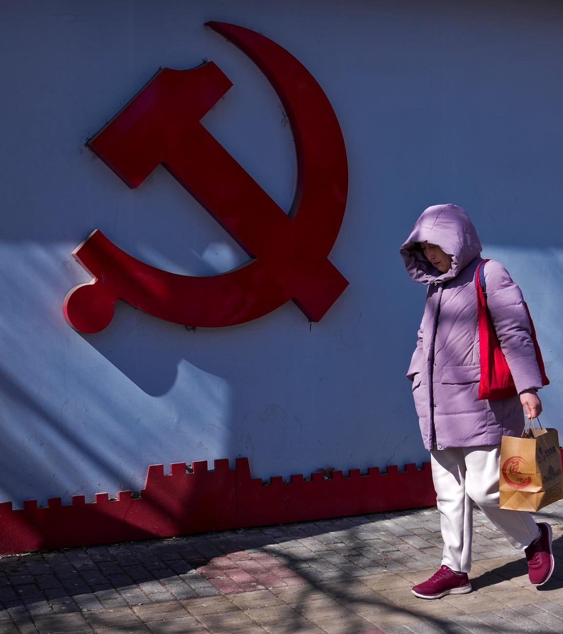 Frau läuft an dem Logo der kommunistischen Partei vorbei