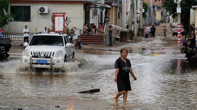 Eine Frau geht durch eine überflutete Straße nach starkem Regen im Bezirk Miyun am Stadtrand von Peking, China.