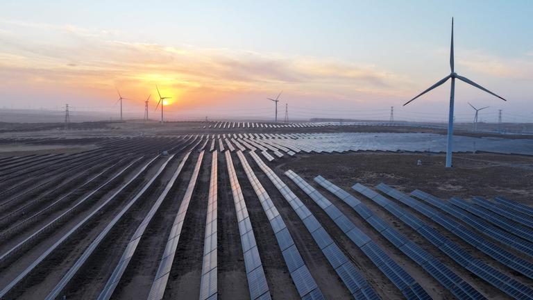 ELuftaufnahme einer Ebene mit Solaranlagen und Windrädern.