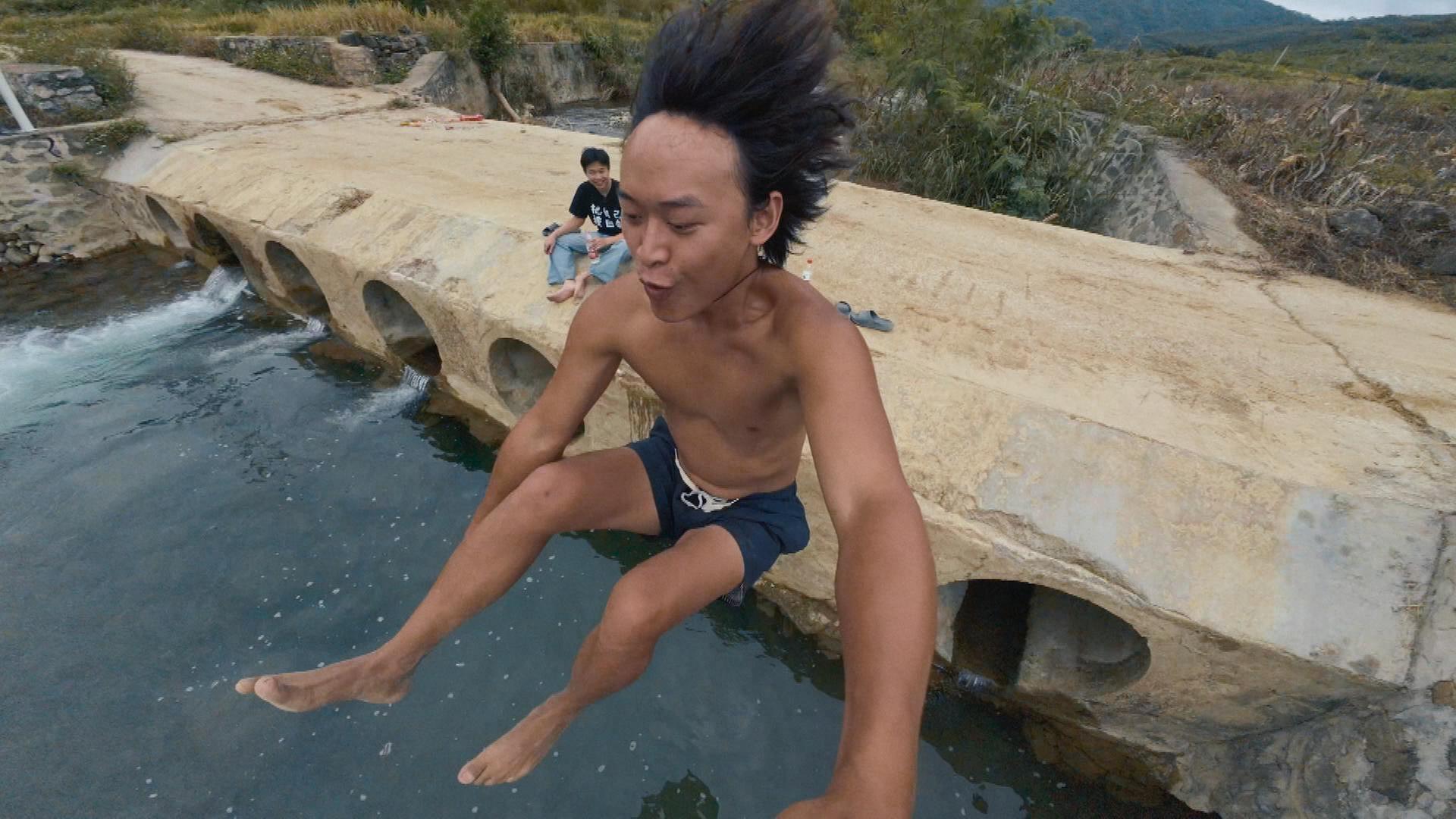 Ein junger Chinese springt mit Kamera in der Hand ins Wasser.
