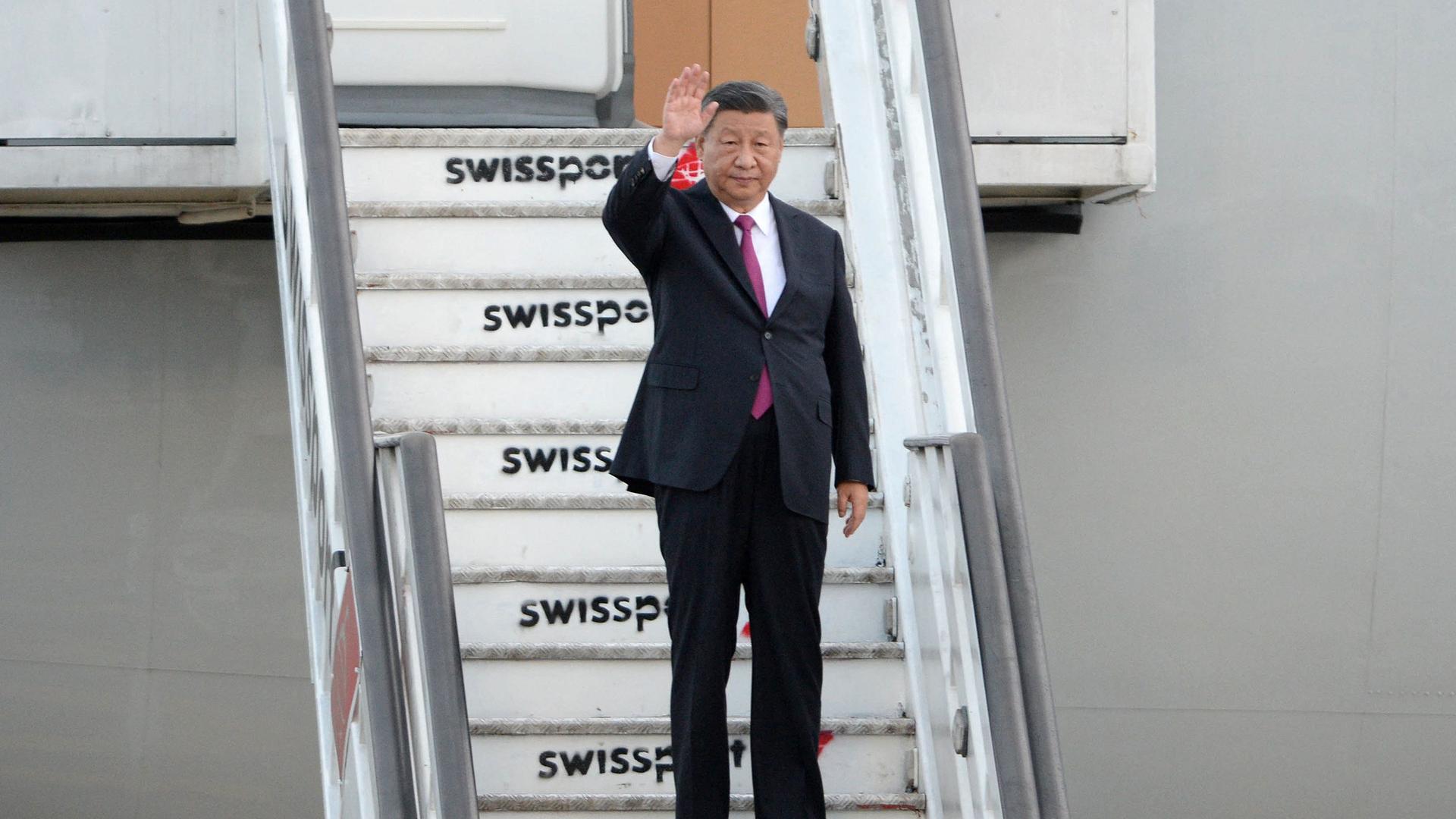 Chinas Staatsoberhaupt Xi Jinping steht auf den Treppen eines Flugzeugs und winkt.