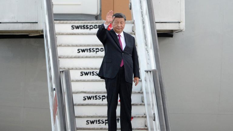 Chinas Staatsoberhaupt Xi Jinping steht auf den Treppen eines Flugzeugs und winkt.