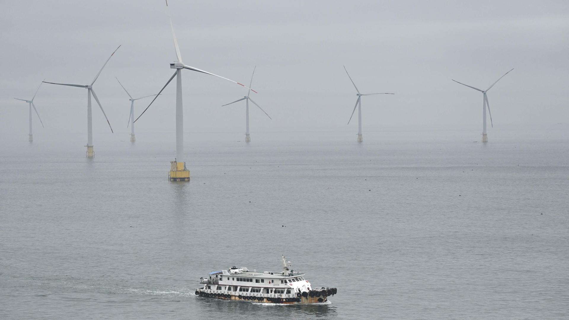 Ein Boot im chinesischen Meer im Hintergrund eine Windparkanlage.