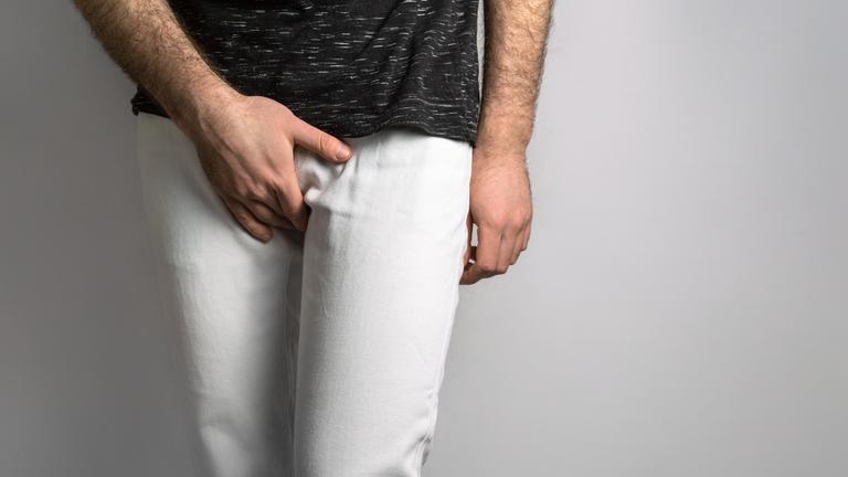 Ein Mann fasst sich in den Schritt.