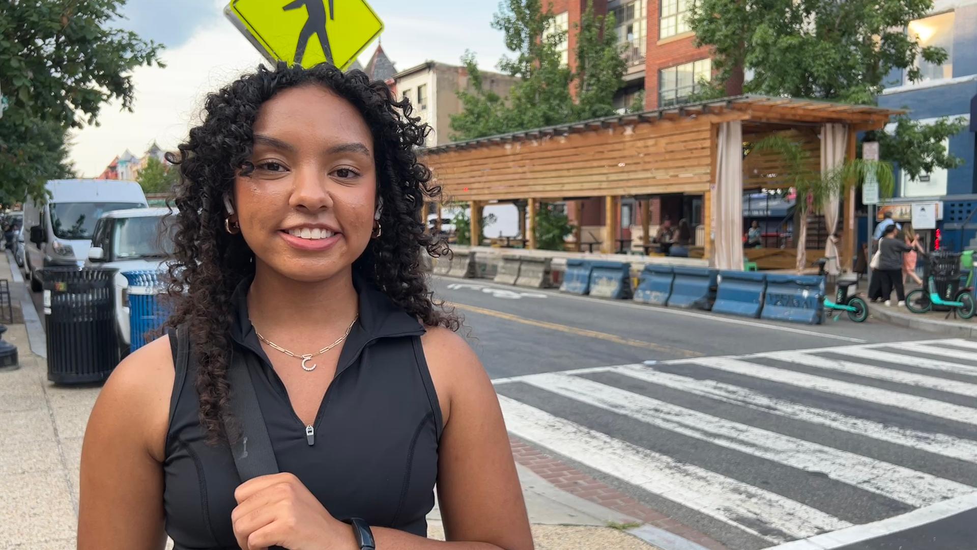Eine junge schwarze Frau steht in einem sportlichen Outfit an einer Kreuzung. 