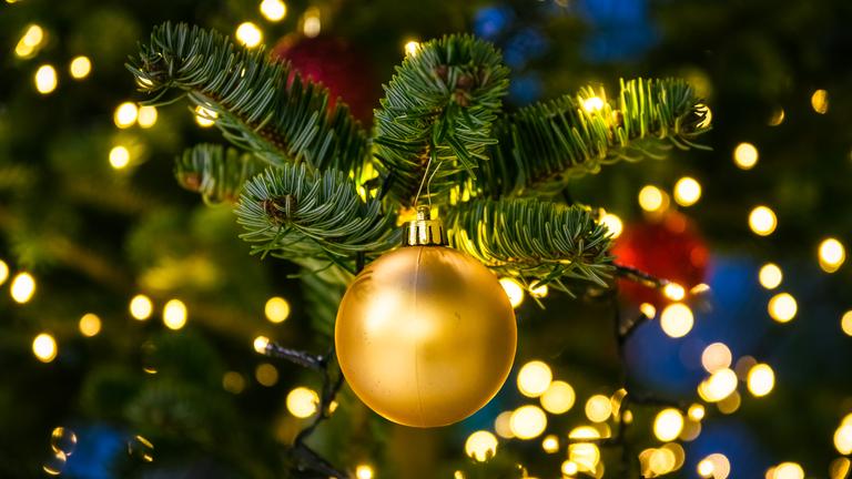 Geschmückter Weihnachtsbaum mit Kugeln und Lichterkette, im Fokus liegt dabei eine goldene Kugel