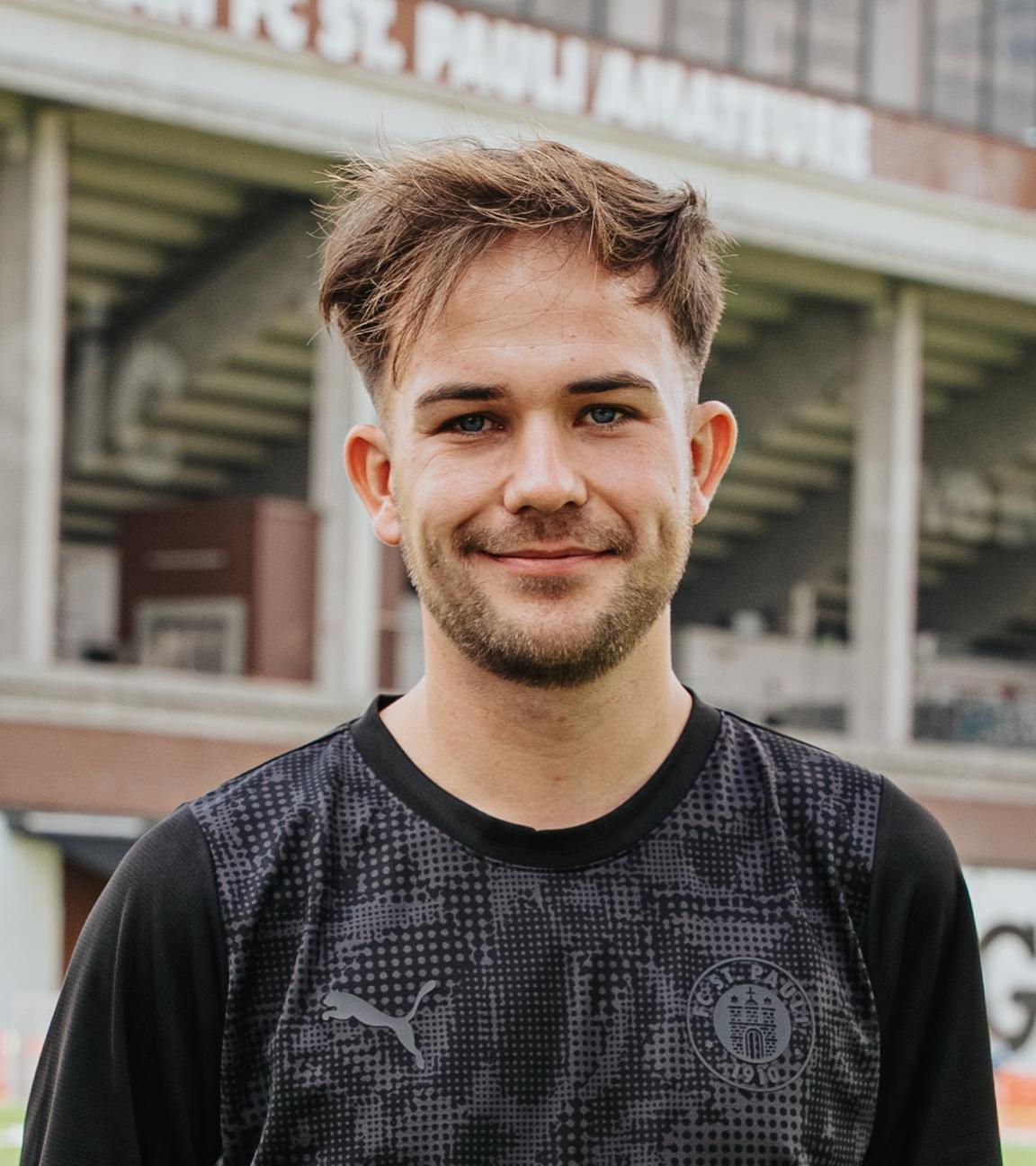 Das Bild zeigt St. Paulis Nachwuchstrainer Christian Dobrick. Er trägt ein schwarzes Fußballtrikot und lächelt in die Kamera.