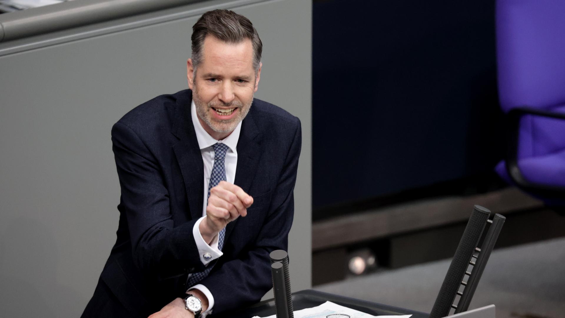 Christian Dürr lehnt am Rednerpult des Bundestags und zeigt mit dem rechten Zeigefinger ins Publikum.