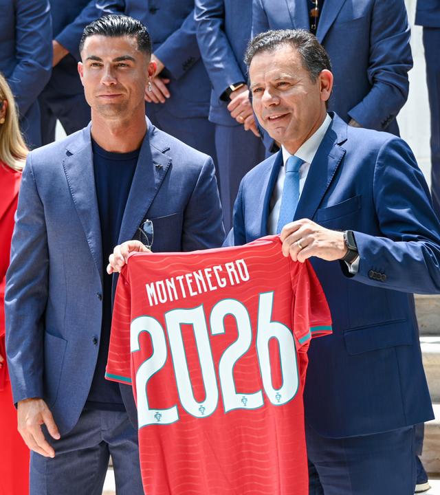 Portugals Premierminister Luis Montenegro hält ein Trikot mit seinem Namen in die Höhe, links neben ihm steht Christiano Ronaldo