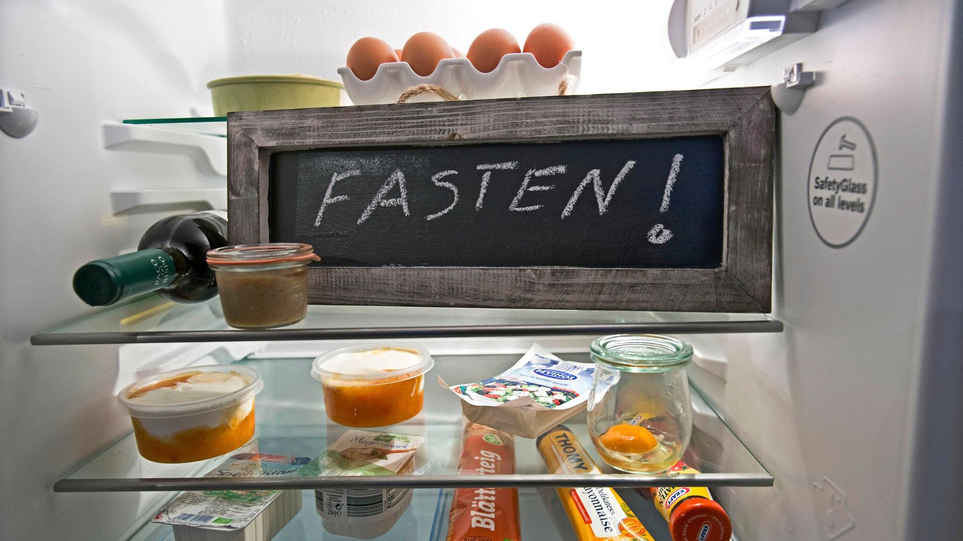 Eine Tafel mit der Aufschrift "Fasten!" steht in einem Kühlschrank mit Lebensmitteln.