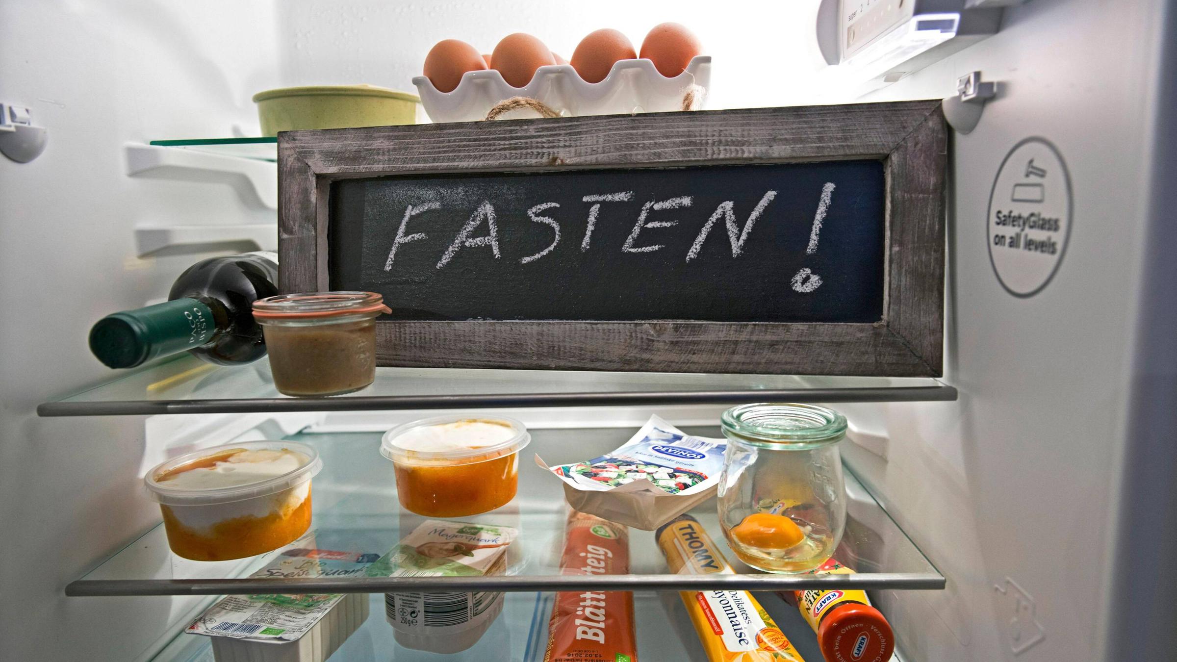 Eine Tafel mit der Aufschrift "Fasten!" steht in einem Kühlschrank mit Lebensmitteln.