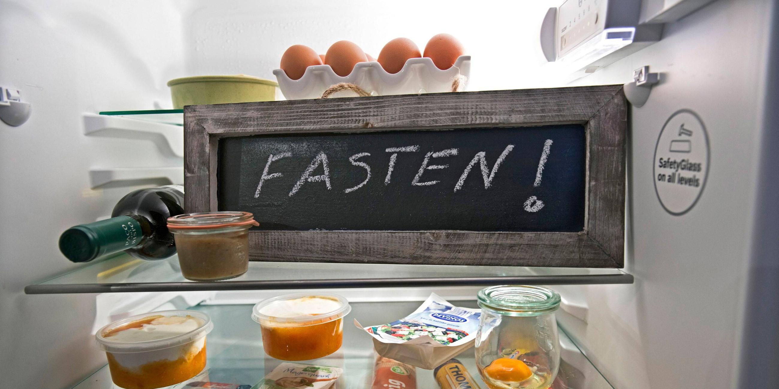 Eine Tafel mit der Aufschrift "Fasten!" steht in einem Kühlschrank mit Lebensmitteln.
