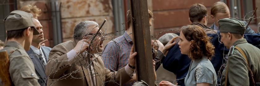 "ZDFzeit: Ein Tag im August - Mauerbau '61": Menschen, getrennt durch Stacheldraht, darunter eine junge Frau, Ingrid Taegner (Sandija Dovgāne), zwischen Grenzsoldaten, die einen älteren Mann auf der anderen Seite des provisorischen Zauns anschaut.