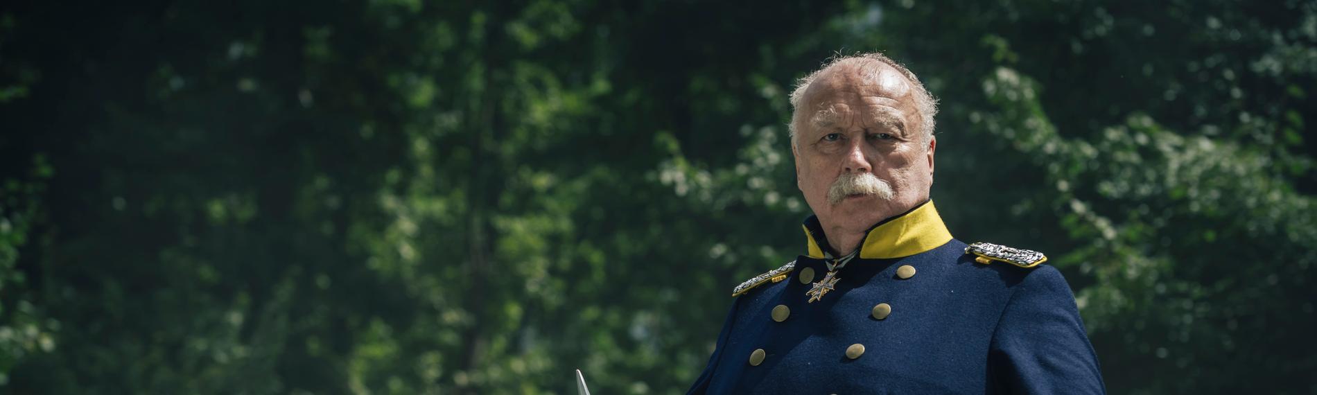 "Kaiserspiel": Spielszene: Otto von Bismarck (Thomas Thieme) in Uniform, im rechten Arm hält er seinen Helm.