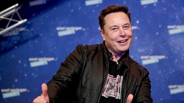 "The True Story of Elon Musk": Elon Musk steht vor einer blauen Wand und zeigt zwei Daumen hoch in die Kamera.