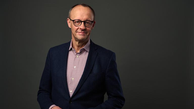 "Mensch Merz! - Der Herausforderer": Großaufnahme des Gesichts von Friedrich Merz vor grauem Hintergrund; er lächelt in die Kamera.