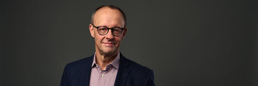 "Mensch Merz! - Der Herausforderer": Großaufnahme des Gesichts von Friedrich Merz vor grauem Hintergrund; er lächelt in die Kamera.