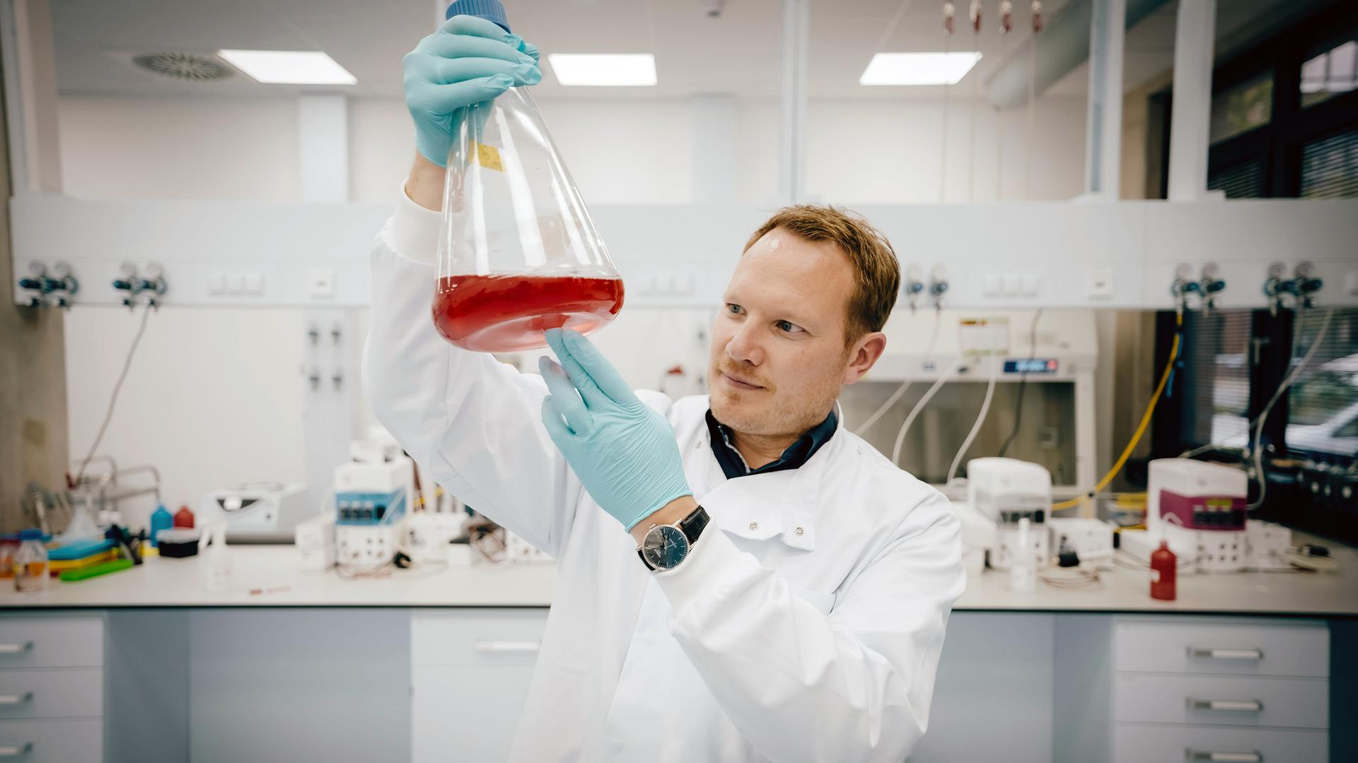 "WISO-Dokumentation: Durchstarten in die Zukunft - Können grüne Start-ups unseren Wohlstand sichern?": Sebastian Rakers steht in seinem Labor. In der Hand hält er einen Glasbehälter, der eine Nährlösung enthält in der Fischzellen wachsen.