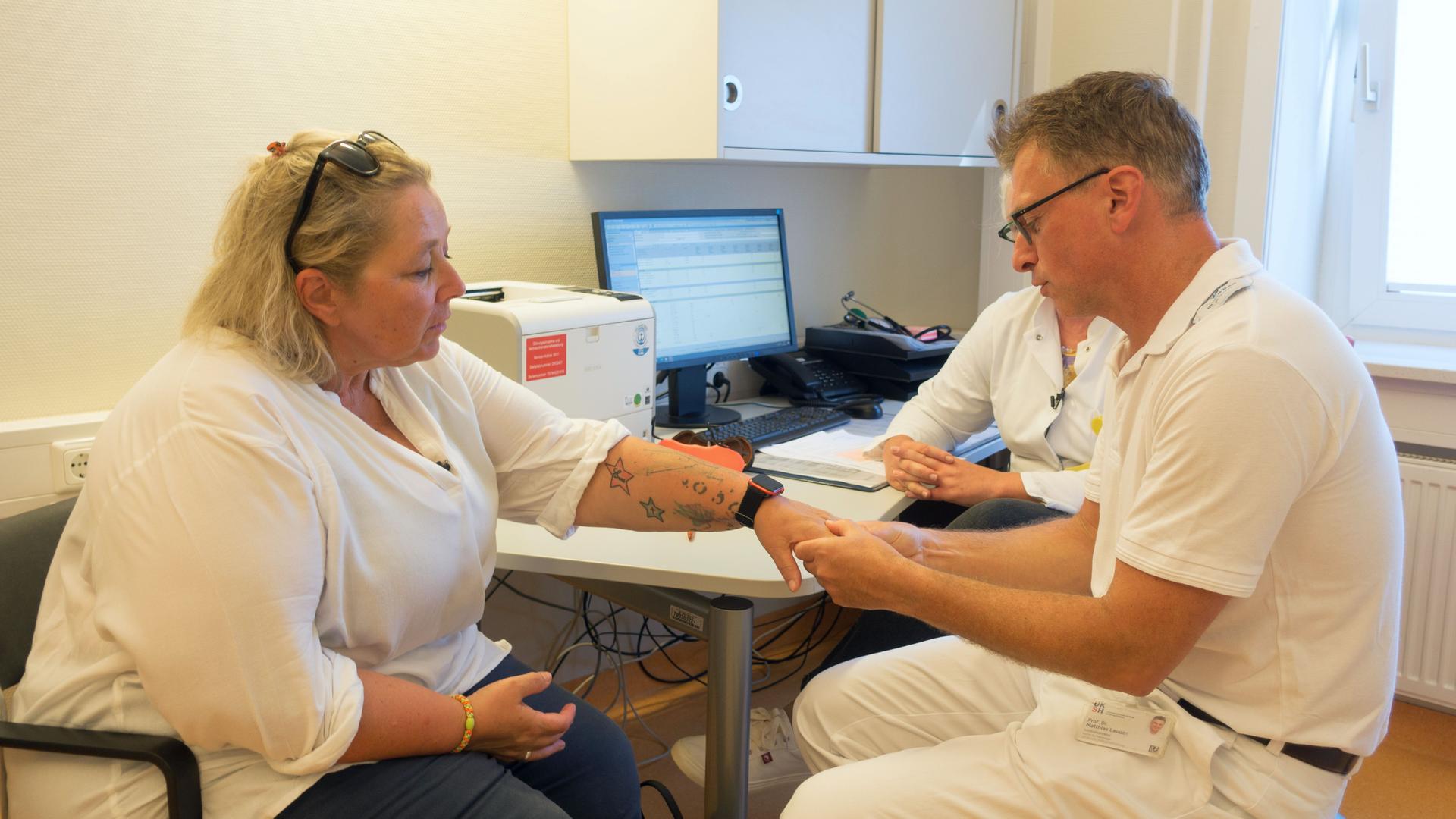 Man sieht eine weibliche Patientin in einer Arztpraxis, welche soeben von einem männlichen Arzt behandelt wird.