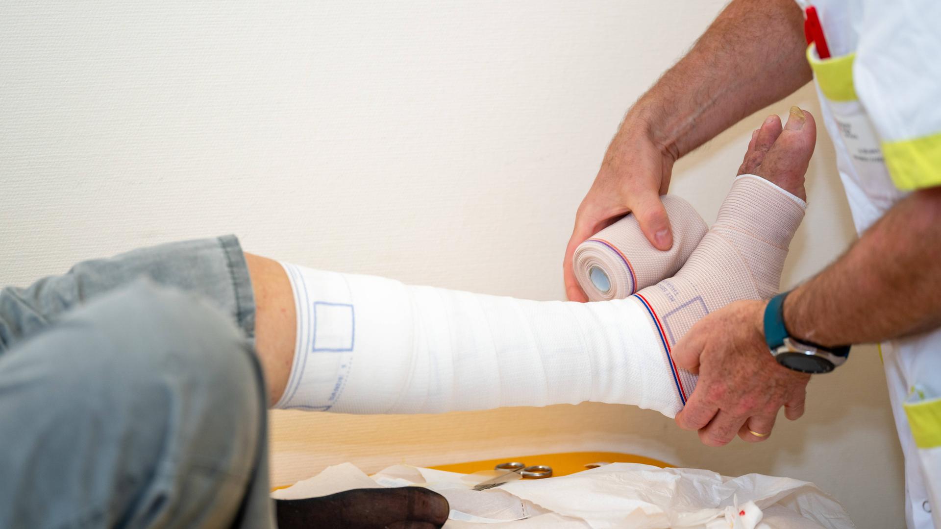 Ein Patient erhält von einem Arzt einen Verband für eine chronische Fußwunde.