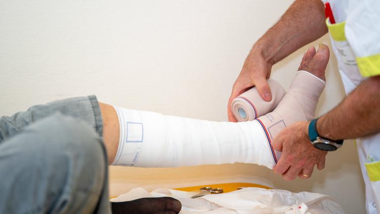 Ein Patient erhält von einem Arzt einen Verband für eine chronische Fußwunde.