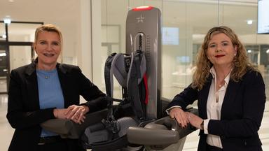 Die zwei Entwicklerinnen Claudia Sodha (l.) und Sabrina Hellstern stehen auf beiden Seiten des Roboters haben ihre Unterarme aufgelegt.