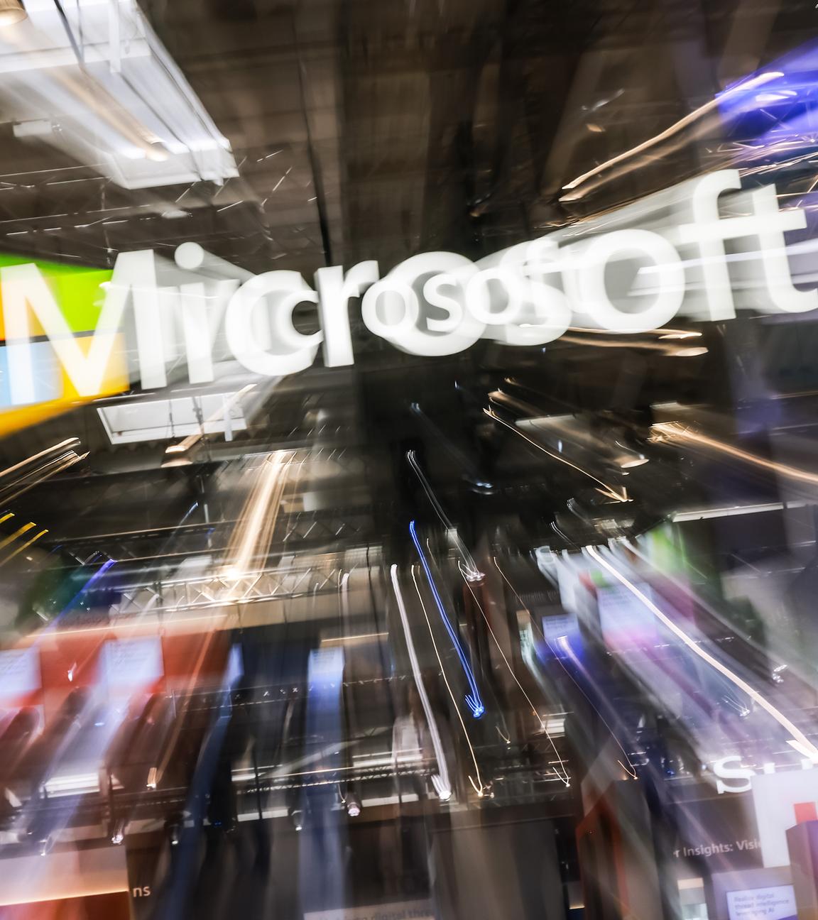 Dynamisch verzerrtes Microsoft-Logo in einem Messeumfeld; der Zoom-Effekt erzeugt einen Strudel aus Licht und Bewegung um das Firmenzeichen.