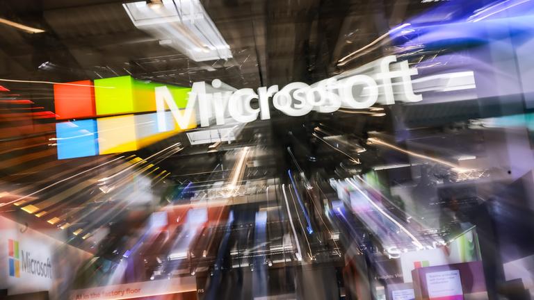 Dynamisch verzerrtes Microsoft-Logo in einem Messeumfeld; der Zoom-Effekt erzeugt einen Strudel aus Licht und Bewegung um das Firmenzeichen.