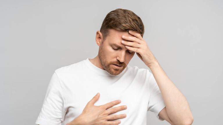 Ein Mann mittleren Alters fühlt sich schlecht. Er legt die Hände auf die Brust und den Kopf mit Kopfschmerzen.