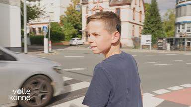 Ein Junge, der ein Cochlea‑Implantat trägt, und gerade die Straße überqueren möchte.