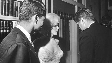 Schwarz-Weiß-Foto: Marilyn Monroe steht zusammen mit John F. Kennedy und Robert Kennedy auf einer Party.
