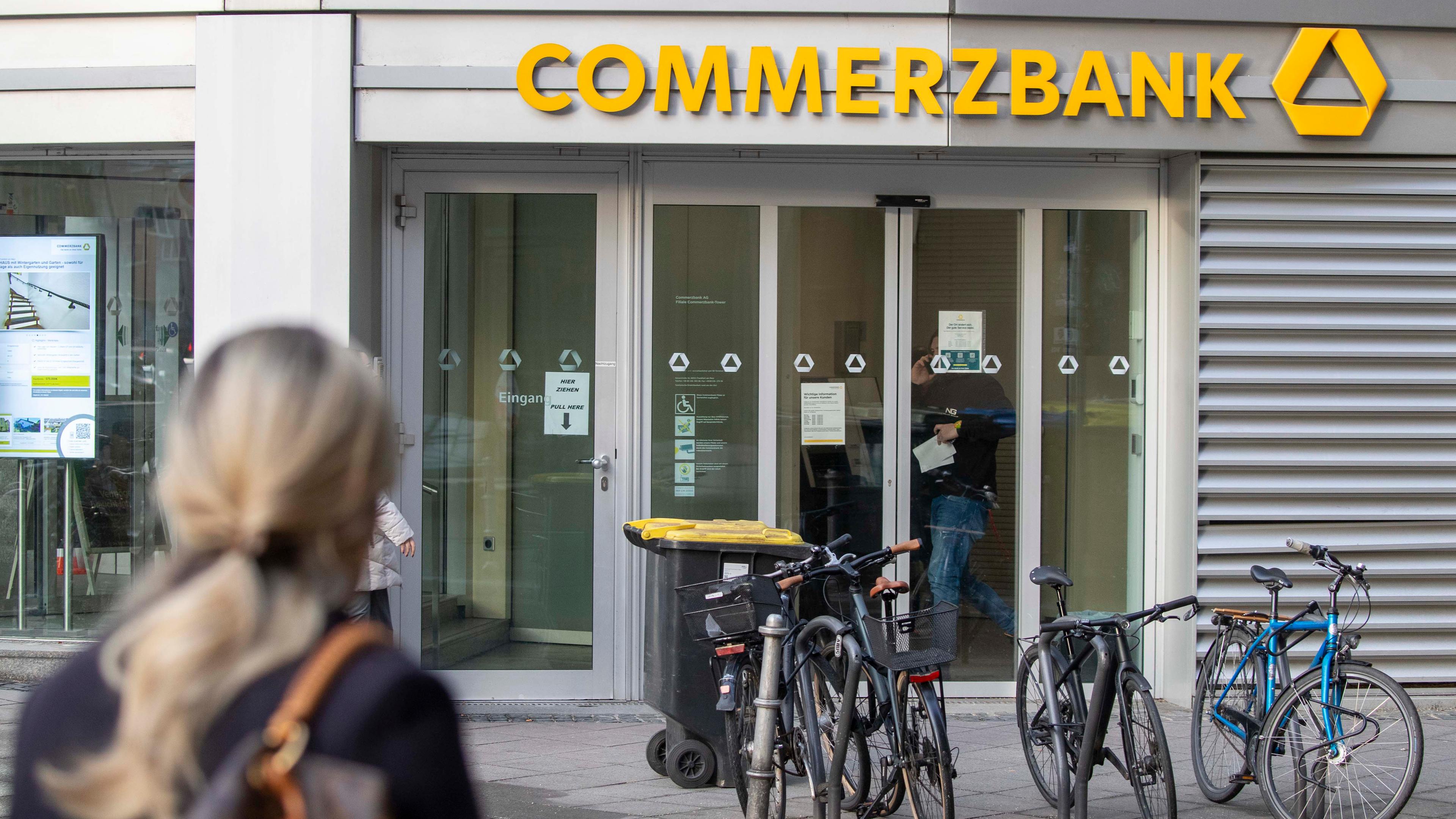 Eine Frau ist im Vordergrund und schaut auf den Eingang einer Commerbank Filiale im Hintergrund.