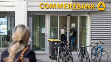 Eine Frau ist im Vordergrund und schaut auf den Eingang einer Commerbank Filiale im Hintergrund.