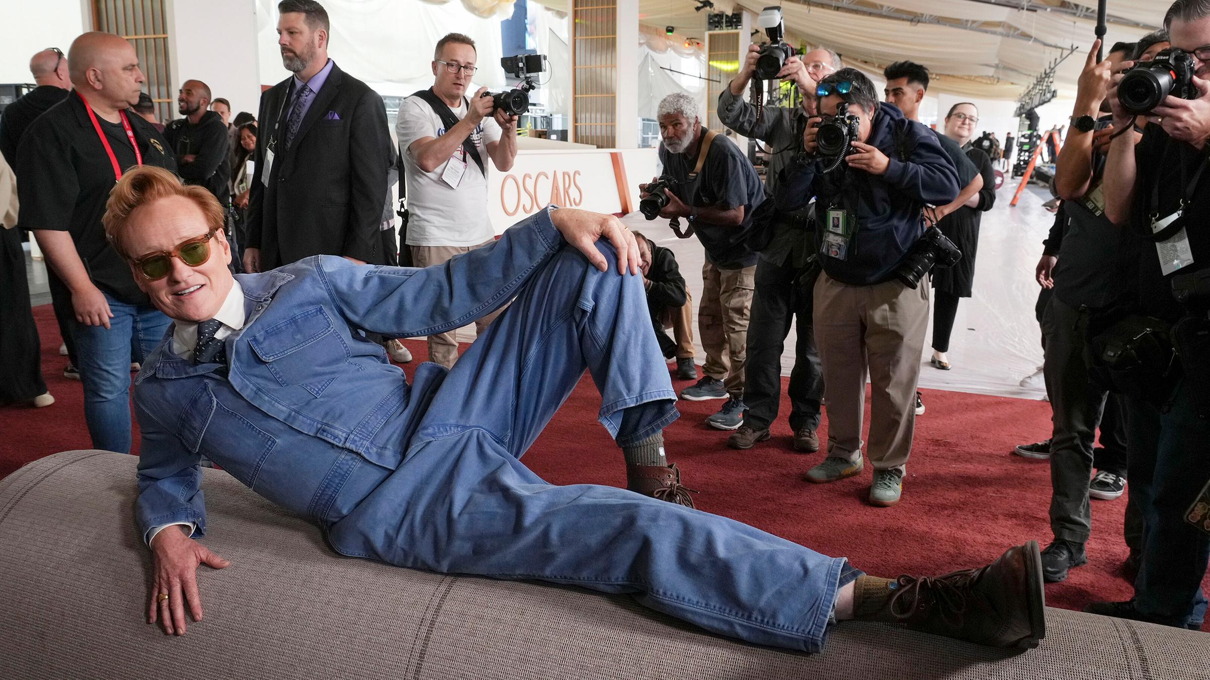 Oscar-Moderator Conan O'Brien posiert auf dem Boden vor dem Oscar-Teppich für die Kamera.
