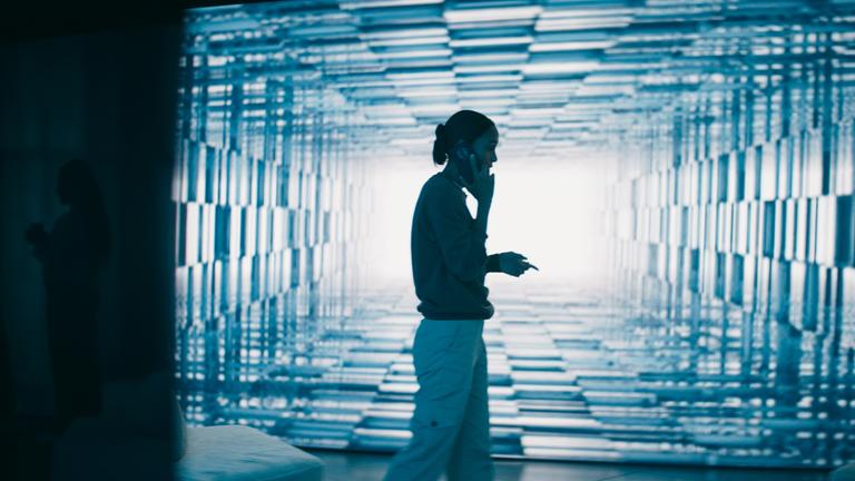 "Concordia - Tödliche Utopie (2) - Der Verdacht": Isabelle Larsson (Nanna Blondell) telefoniert im Laufen vor einer blau leuchtenden Monitorwand.