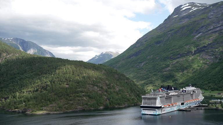 Eine Drohnenaufnahme von dem Kreuzfahrtschiff MSC Euribia im Hafen von Hellesylt im Geiranger Fjord in Norwegen.