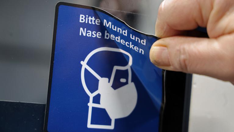 Ein Piktogramm mit dem Hinweis auf Corona-Maskenpflicht wird entfernt.