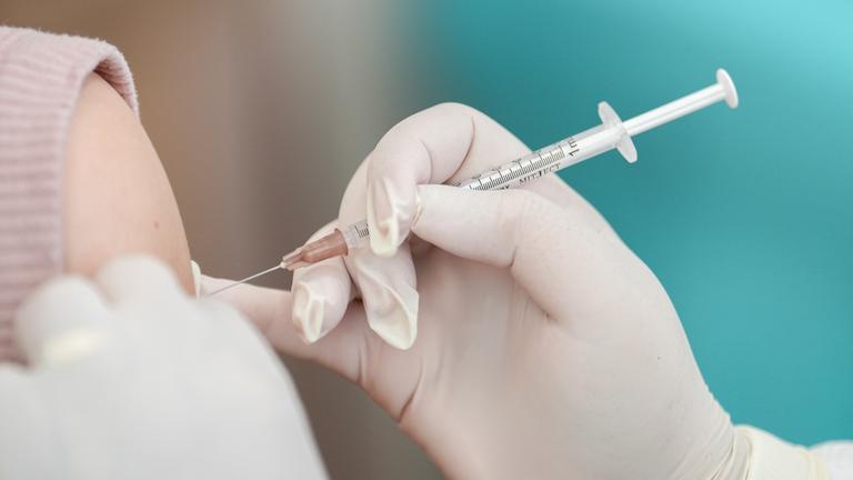 Eine Spritze mit einer Corona-Impfung wird in einen Oberarm verabreicht.