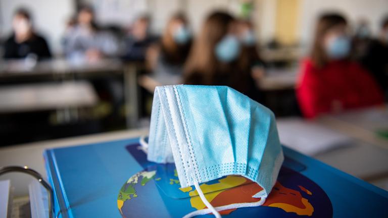 Eine Maske liegt auf einem Atlas in einem Klassenzimmer