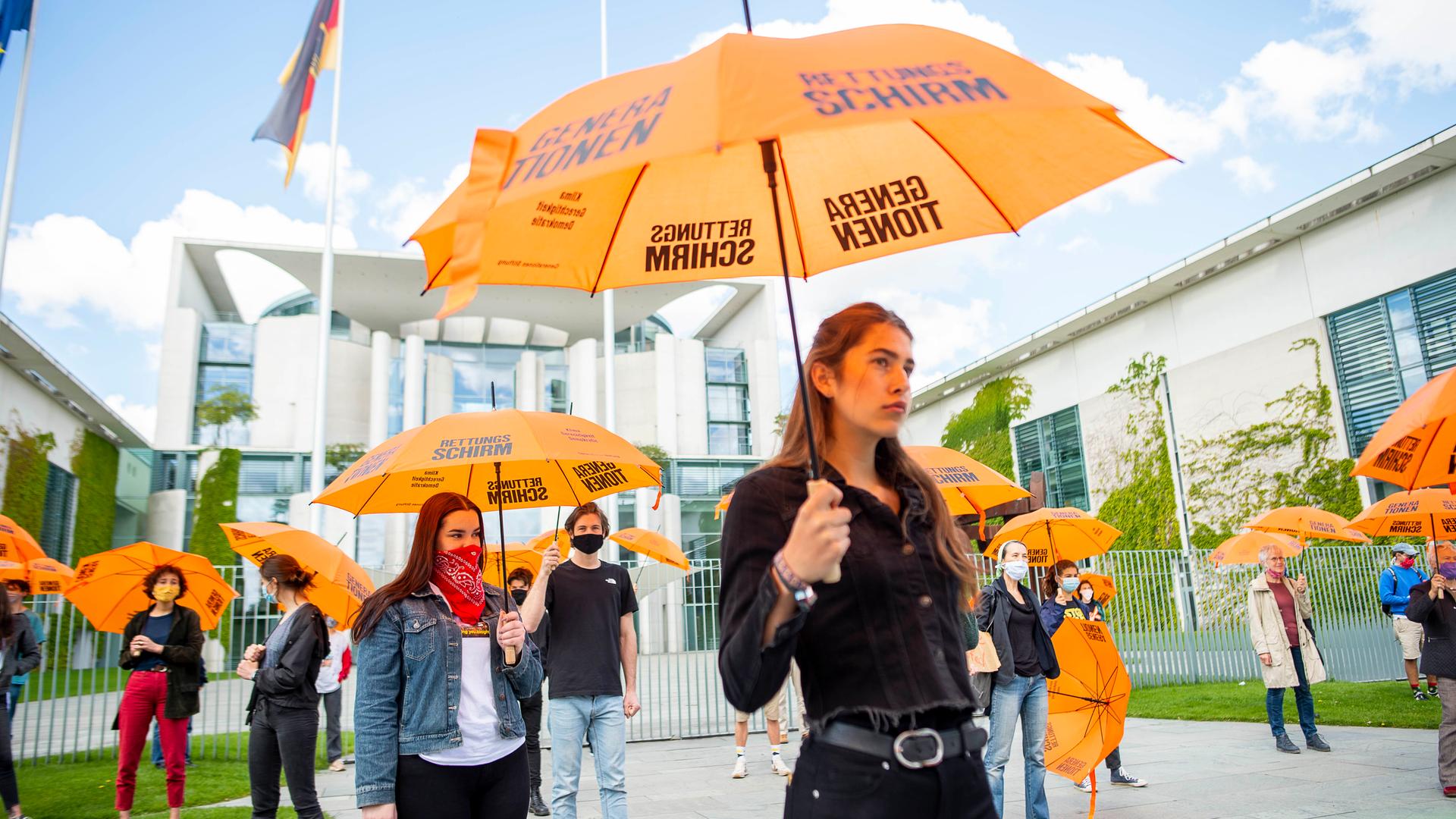 Junge Leute demonstrieren mit Regenschirmen vor dem Kanzleramt für den Generationenrettungsschirm in der Corona-Krise.