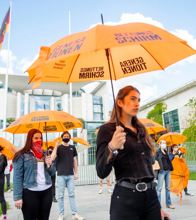 Junge Leute demonstrieren mit Regenschirmen vor dem Kanzleramt für den Generationenrettungsschirm in der Corona-Krise.