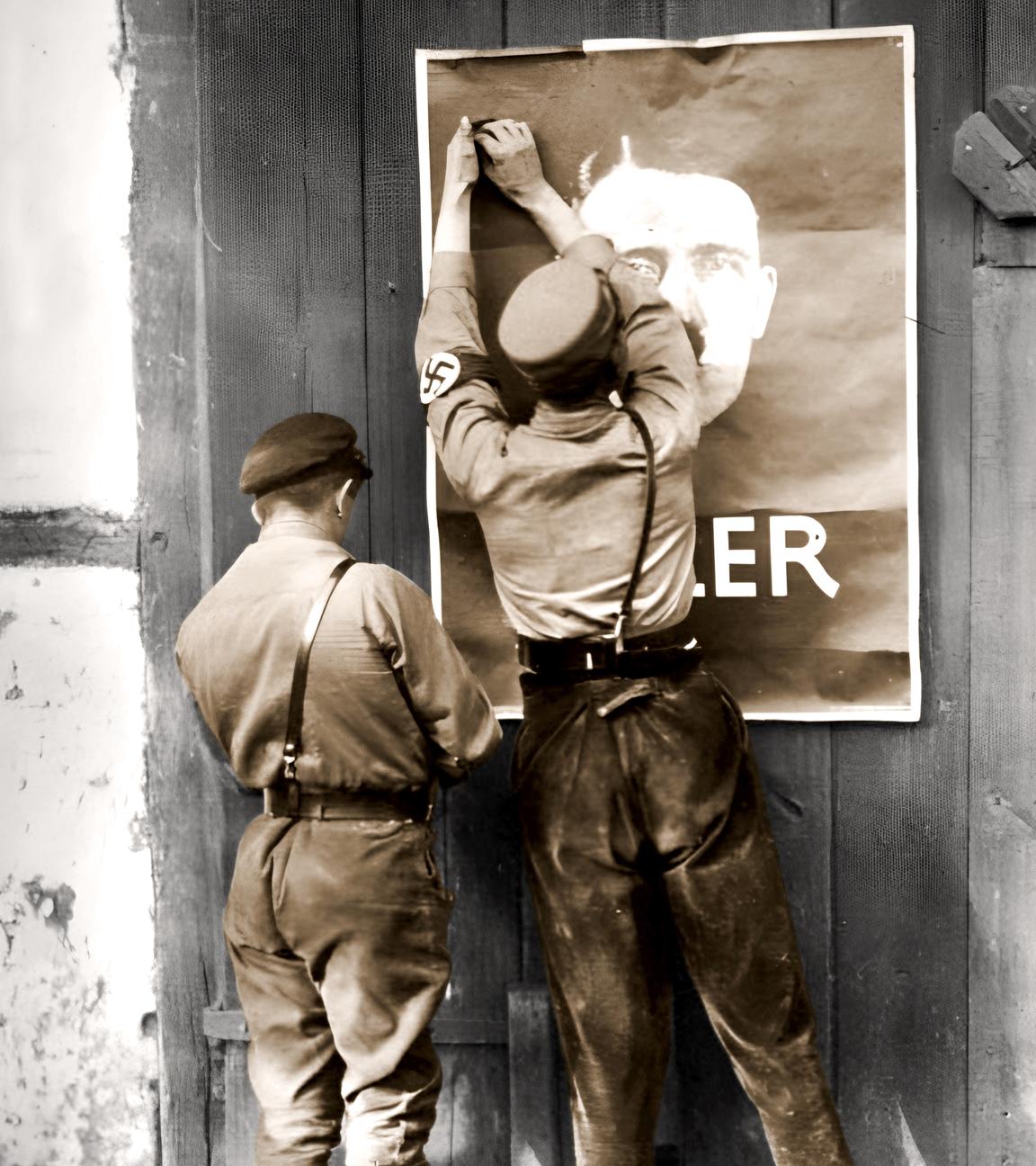 Junge Nationalsozialisten befestigen ein Wahlplakat für Hitler an einer Scheunentür.