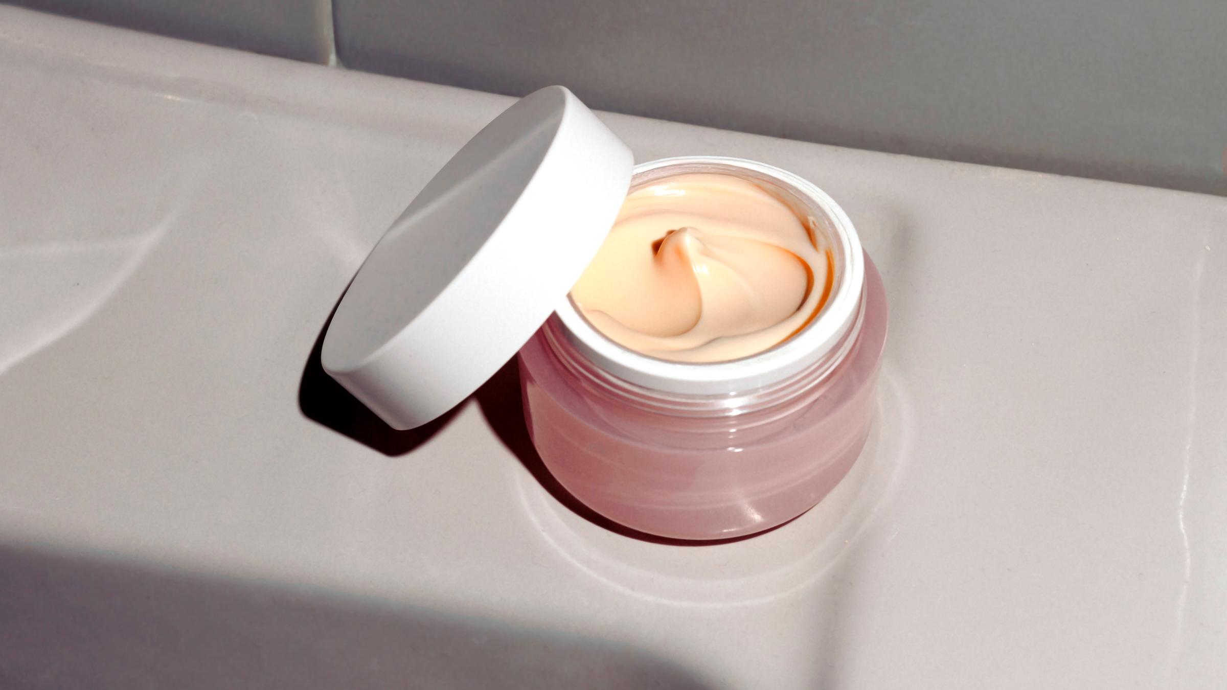 Ein geöffneter Cremetiegel mit Inhalt steht im Badezimmer.