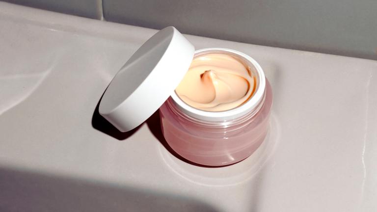 Ein geöffneter Cremetiegel mit Inhalt steht im Badezimmer.