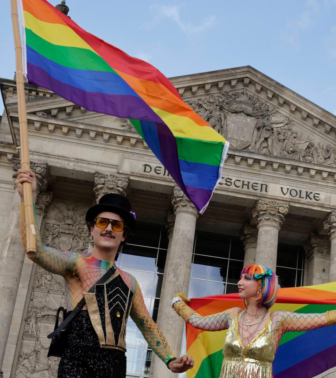 Teilnehmer des Christopher Street Day in Berlin am 26.07.2025 schwenken Regenbogenfahnen vor dem Reichstagsgebäude.