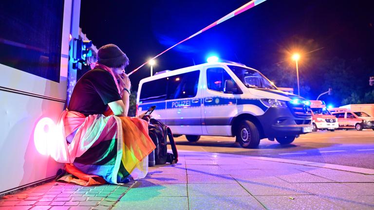Ein Mann in eine Pride-Fahne gehüllt, hockt neben einem Polizeifahrzeug nach dem Abbruch des Christopher Street Day (CSD).