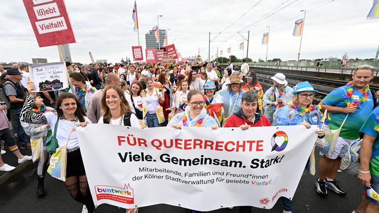 Demonstriende auf dem CSD in Köln. Sie halten ein großes Plakat in der Hand auf dem steht "Für Queerrechte. Viele. Gemeinsam. Stark"