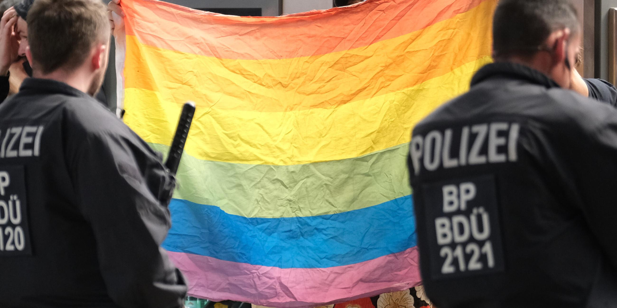 Polizisten stehen vor einer Regenbogenflagge. 