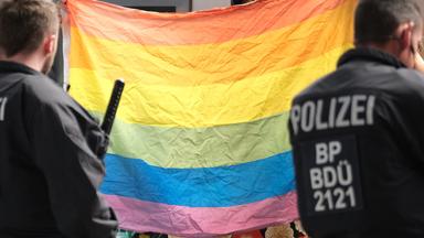 Polizisten stehen vor einer Regenbogenflagge. 