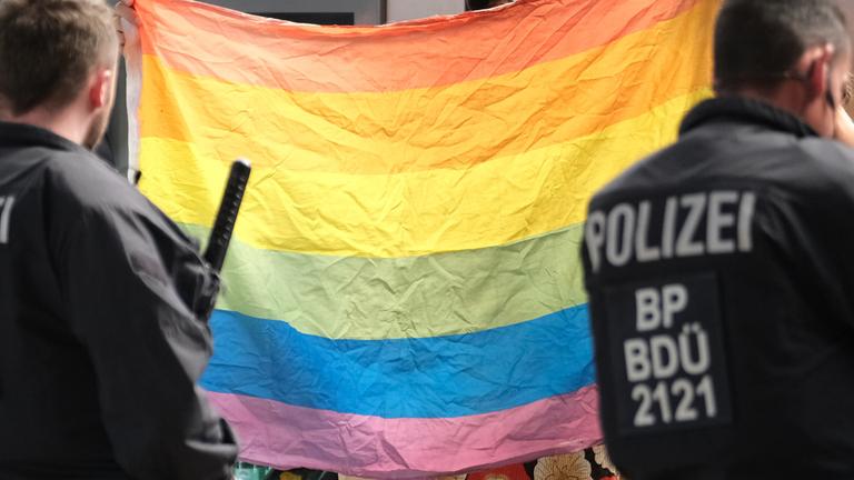 Polizisten stehen vor einer Regenbogenflagge. 